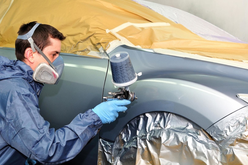 man in protective gear painting a car