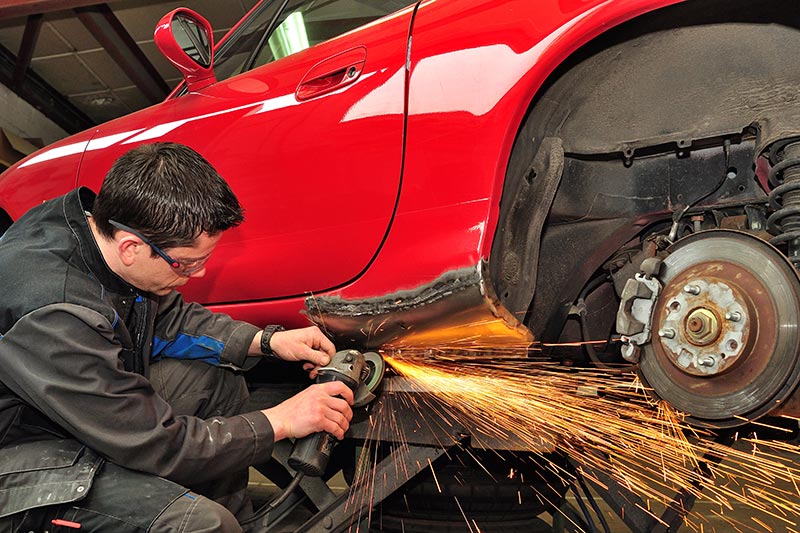 technician repairing the underside of a red car