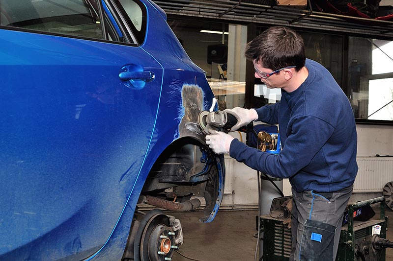 technician wearing blue repairing a the front bumper of a blue car